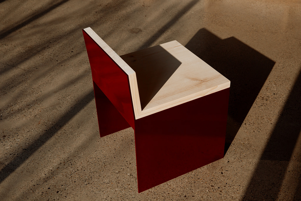 Kalonstudios materialstudies diningchair 2 Abstract Red Wooden Sculpture with a Light Wood Top Forming a V notch on a Sunlit Concrete Floor