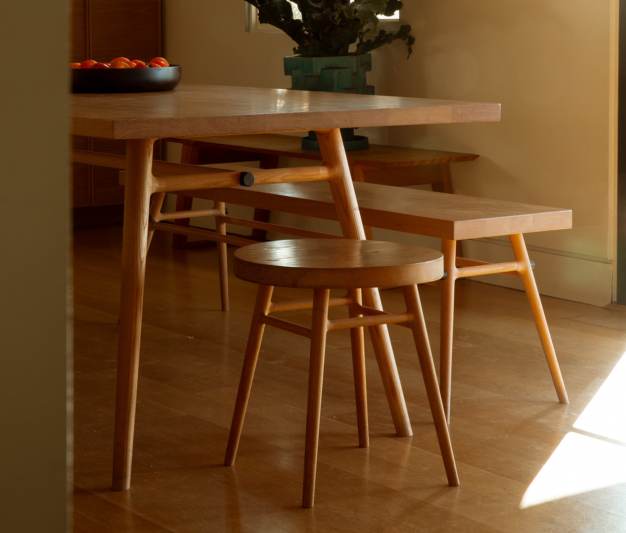 Wooden Dining Table with Matching Stools and a Bench Bathed in Warm Light with Oranges in a Bowl on the Table left |  | Kalon Studios Us