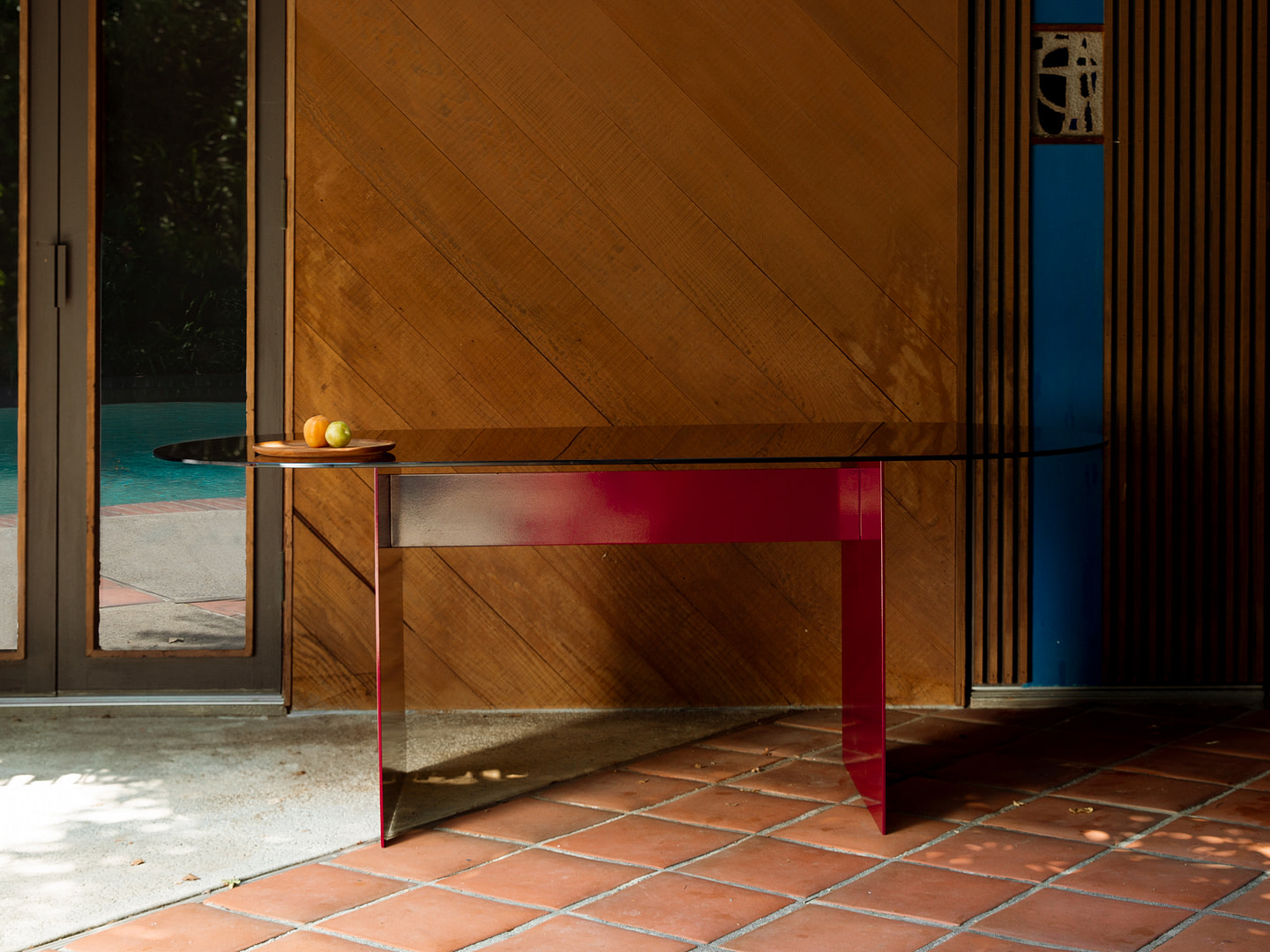 Wood paneled Wall with a Round Glass Table and Pink Legs Fruit on a Brown Plate Doorway to a Pool Area |  | Kalon Studios Us