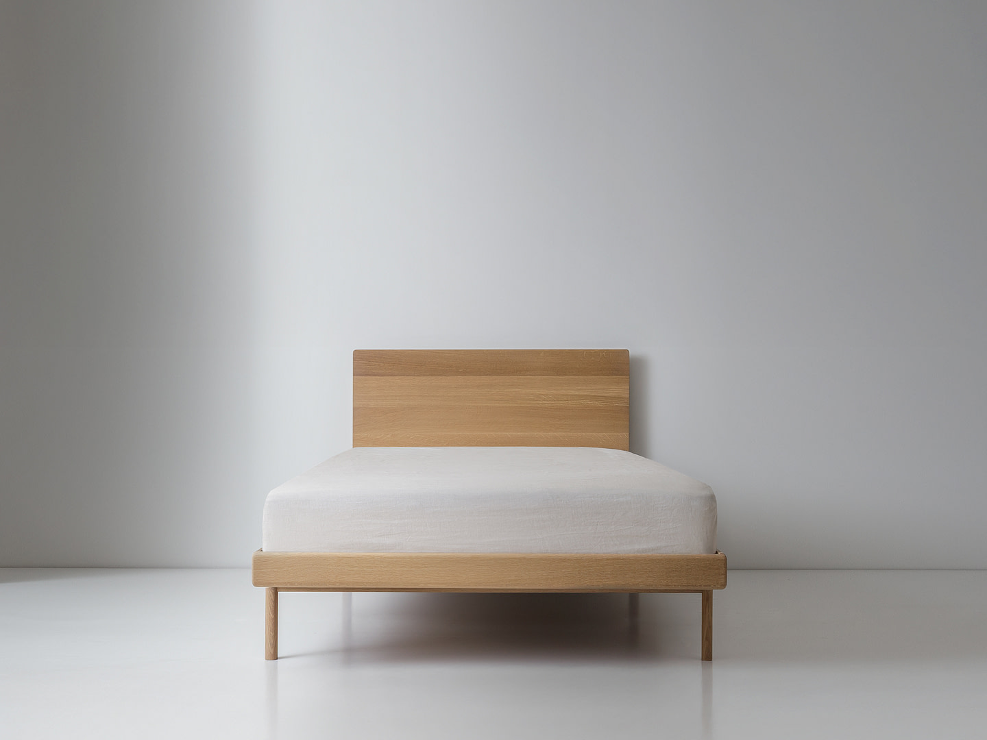 Kalon whiteoak simplebed twin Simple Bed in White Oak with Panel Headboard and White Mattress Plain Wood Legs Centered Front View White Floor