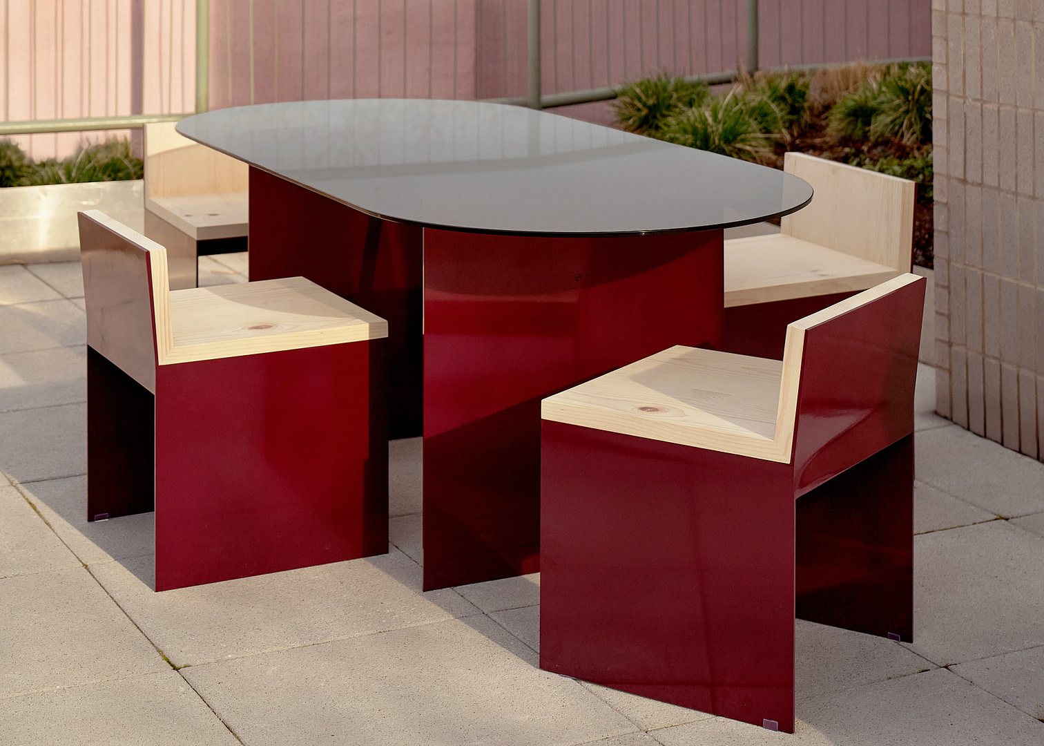 Kalon Material Studies I Aluminum Outdoor Furniture Outdoor Red Furniture Set with a Round Glass top Table and Wooden Benches on a Concrete Patio in an Urban Courtyard