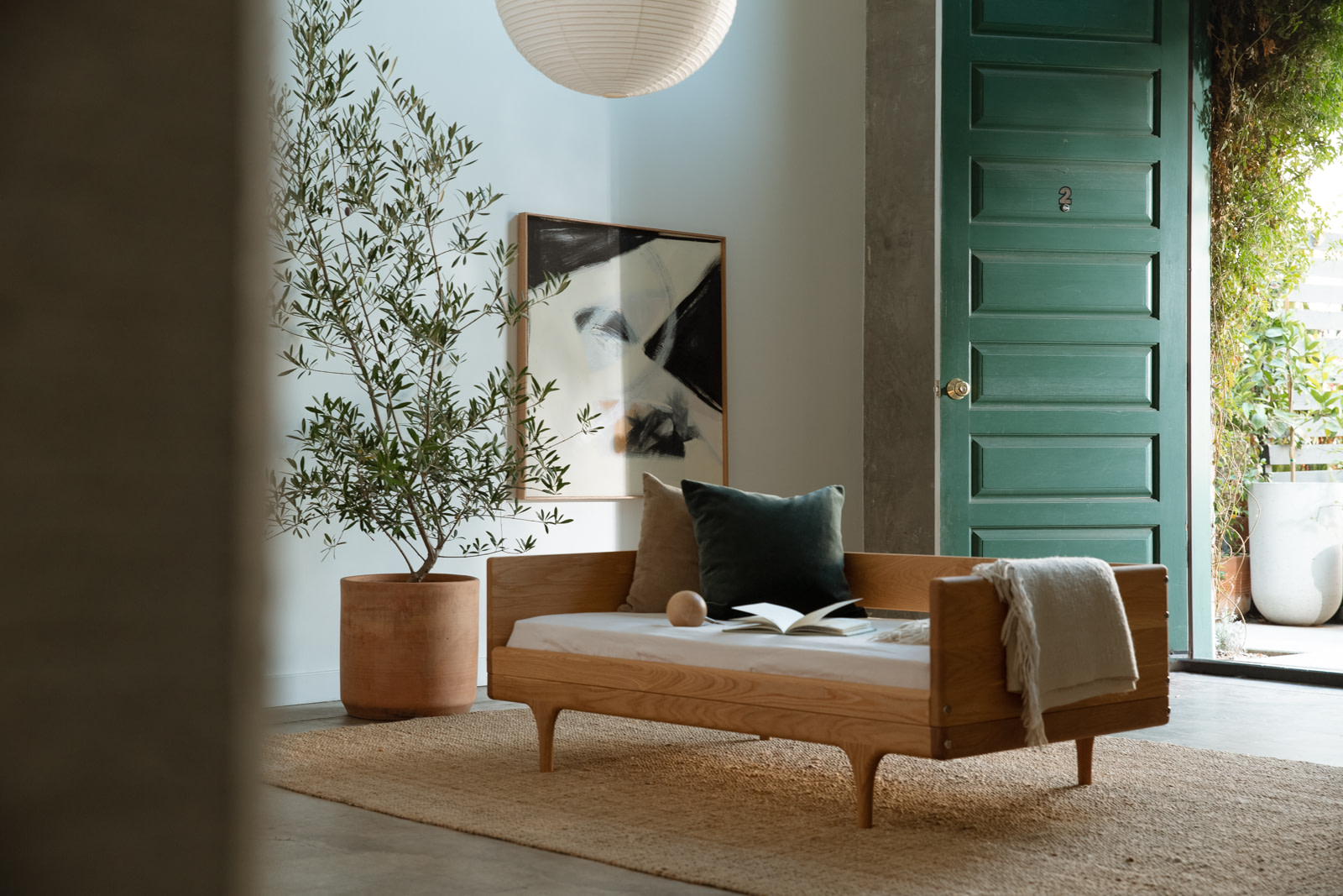Kalonstudios caravan conversionkit naturalfinish 8 Caravan Divan in White Oak in a Sunlit Entryway with Green Paneled Door Paper Lantern Olive Tree in Terracotta Pot