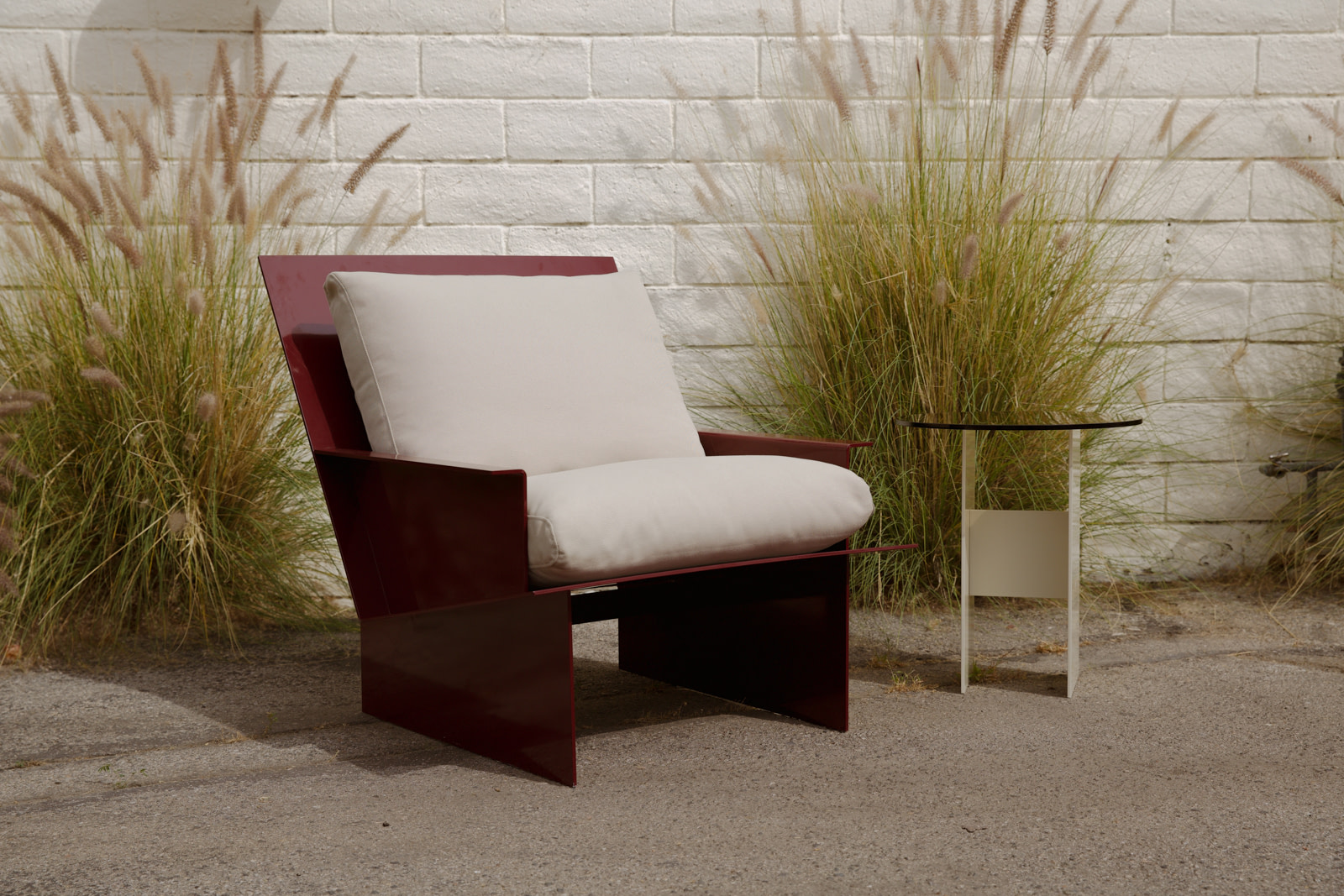 Material Studies I Side Table in lime white beside an oxblood lounge chair, on a planted brick terrace