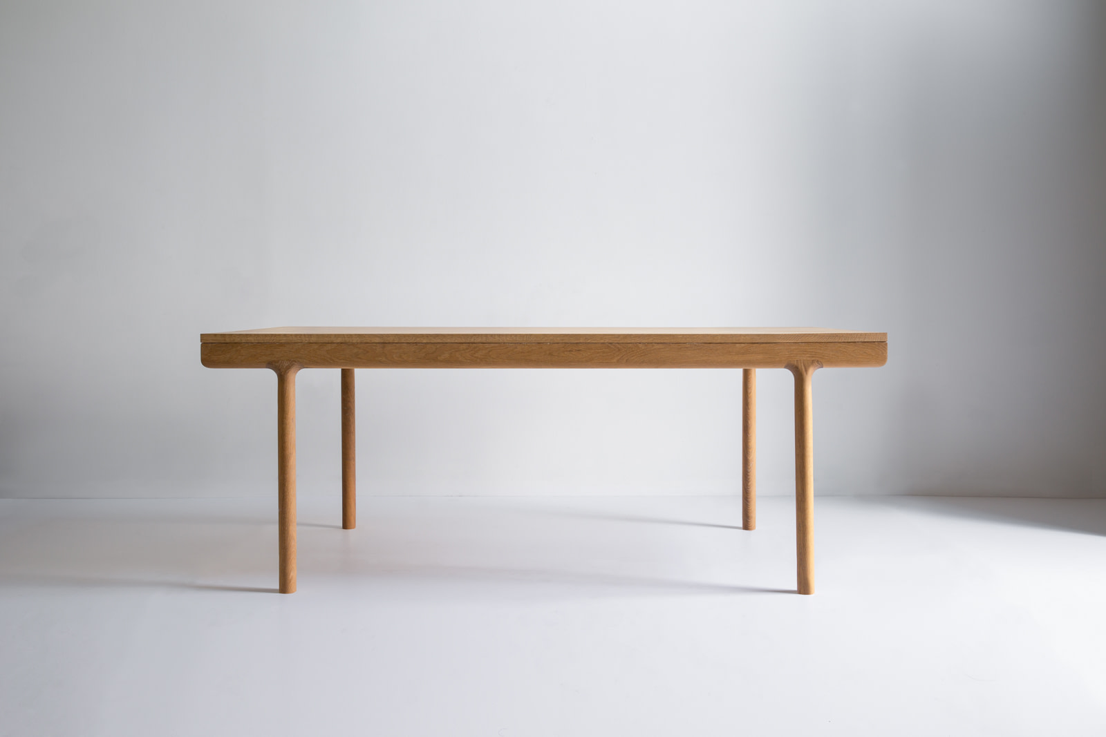 Long Minimalist Wooden Table with Rounded Legs Placed in a Bright Empty Studio |  | Kalon Studios Us