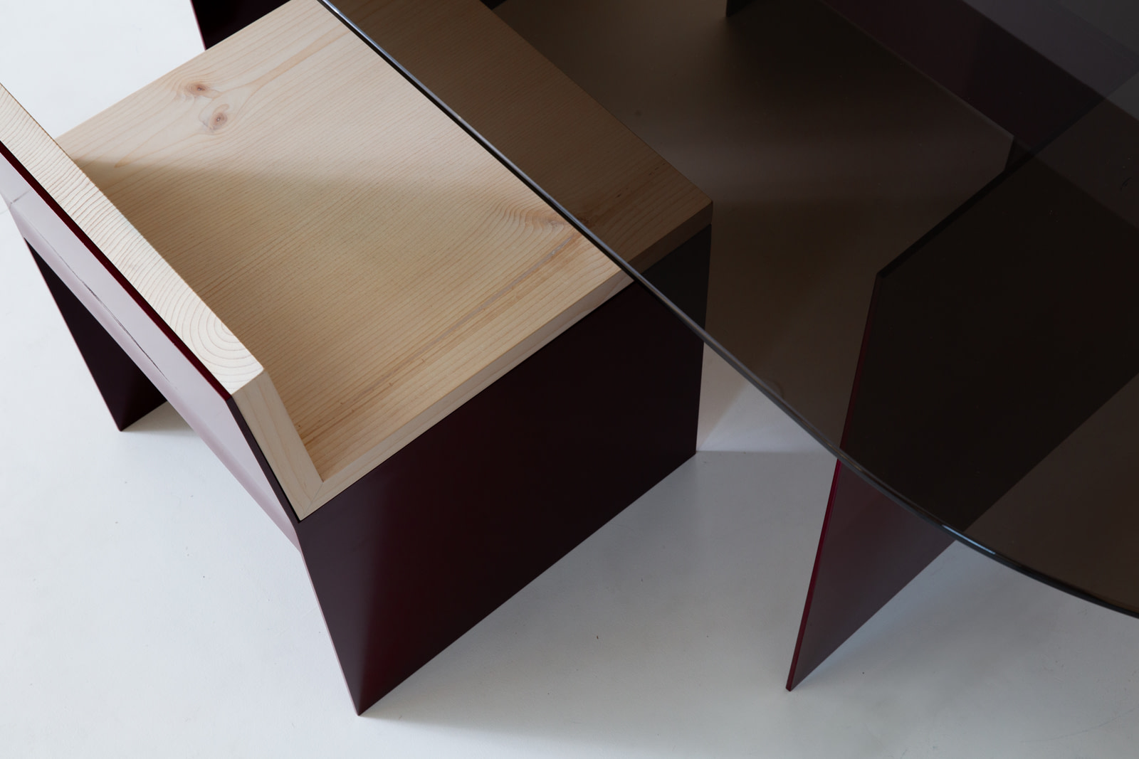 Material Studies I Dining Chair, oxblood aluminum and sugar pine, tucked beneath the smoked-glass dining table