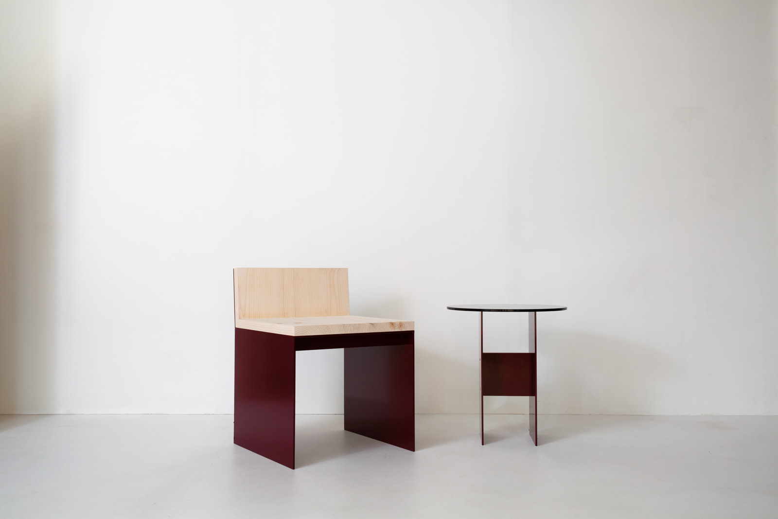 Material Studies I Dining Chair in oxblood aluminum and sugar pine, beside a small oxblood side table