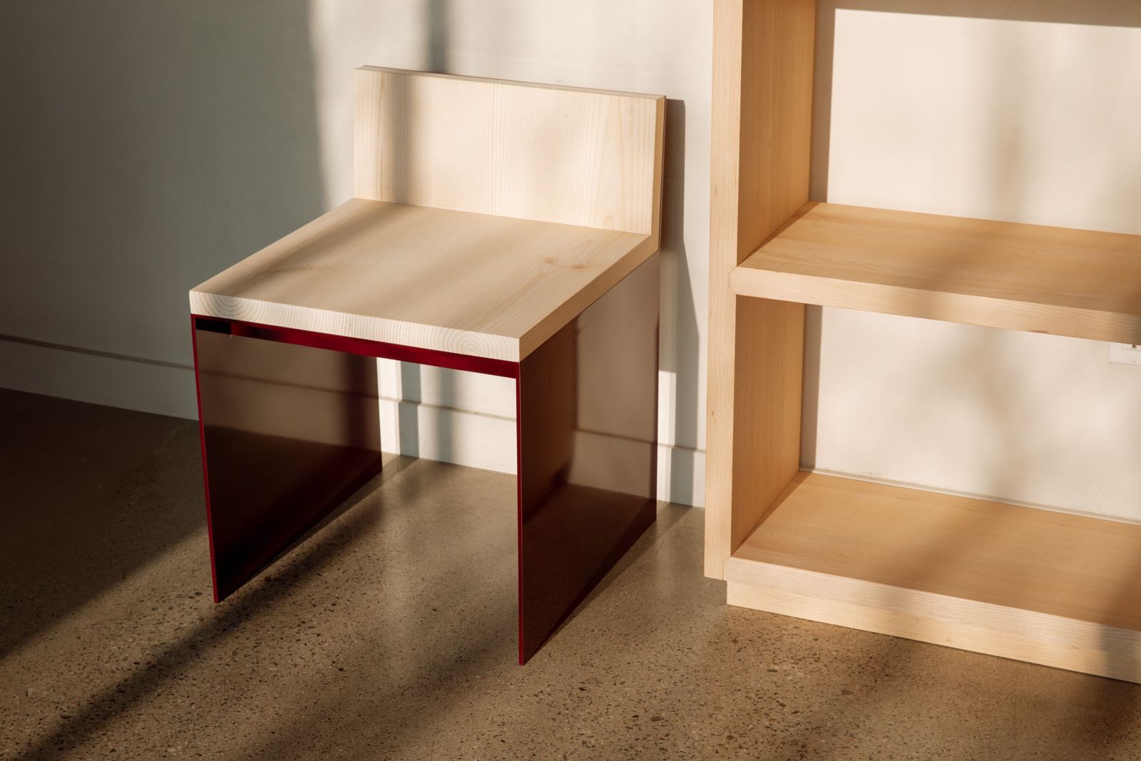 Material Studies I Dining Chair, oxblood aluminum with cantilevered sugar pine seat, side view by a pine shelf