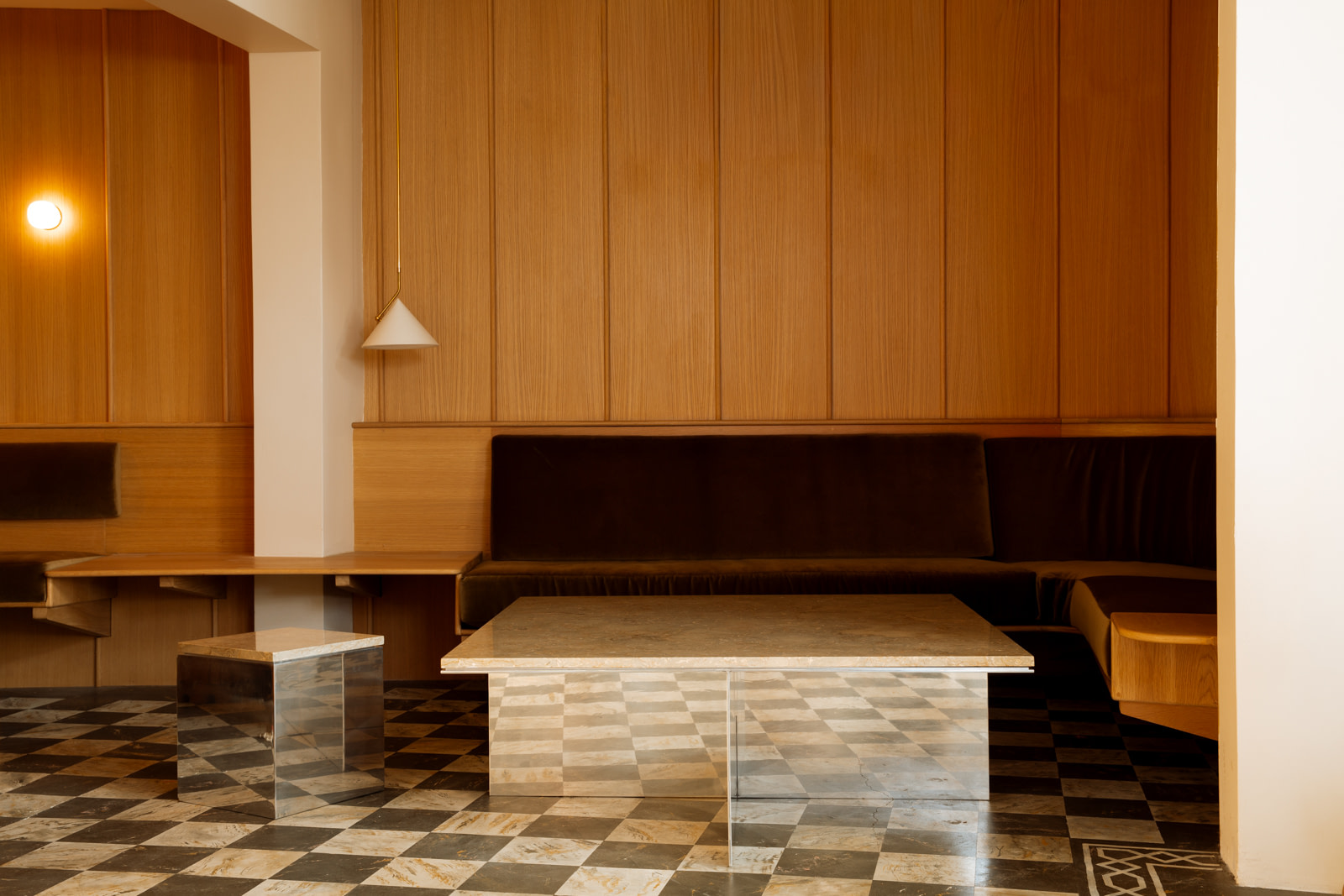 Lounge Area with a Long Brown Leather Couch Against Wood paneled Wall Two Marble Coffee Tables and a Black and white Checkered Floor |  | Kalon Studios Us