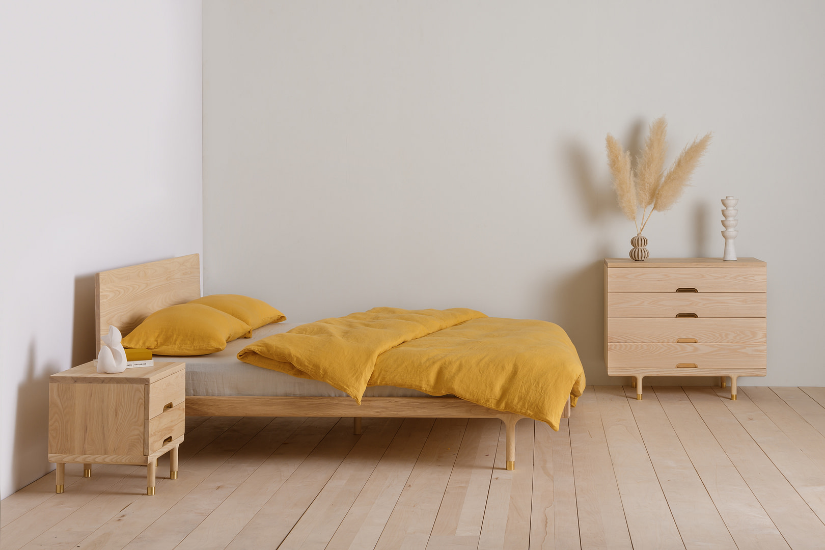 Kalon simplebed ash 7 Simple Bed in Ash with Mustard Bedding Angled Bedroom View with Simple Side Table and Dresser Pampas Grass Plank Floor
