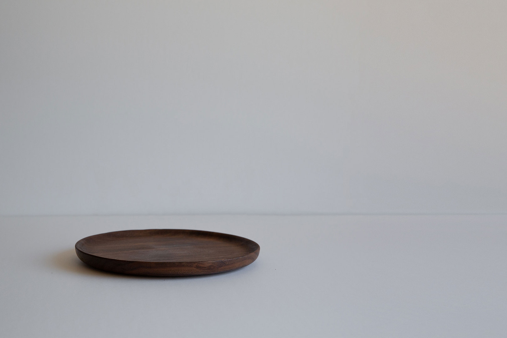 8.5-inch roasted plate in dark wood, empty and seen in profile with a low rim, on a white backdrop.