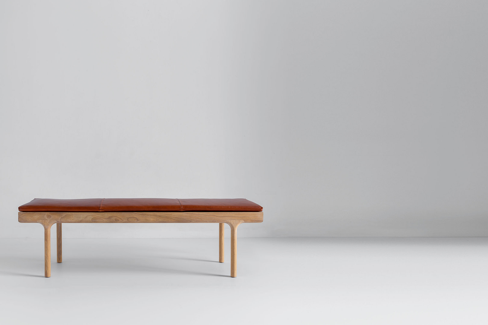 Highland Bench in white oak, cognac leather cushion, three-quarter side in a full-bleed studio frame.