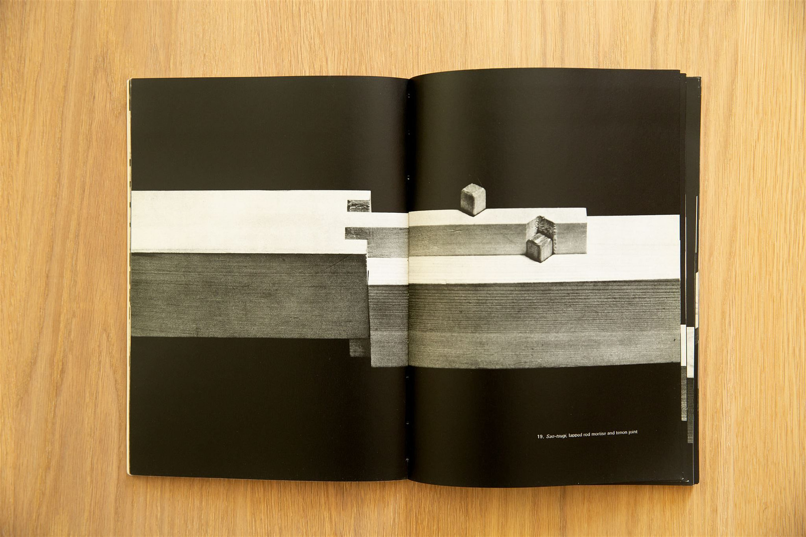 Open book on a wooden table showing a grayscale diagram of a lapped rod mortise and tenon joint on dark pages
