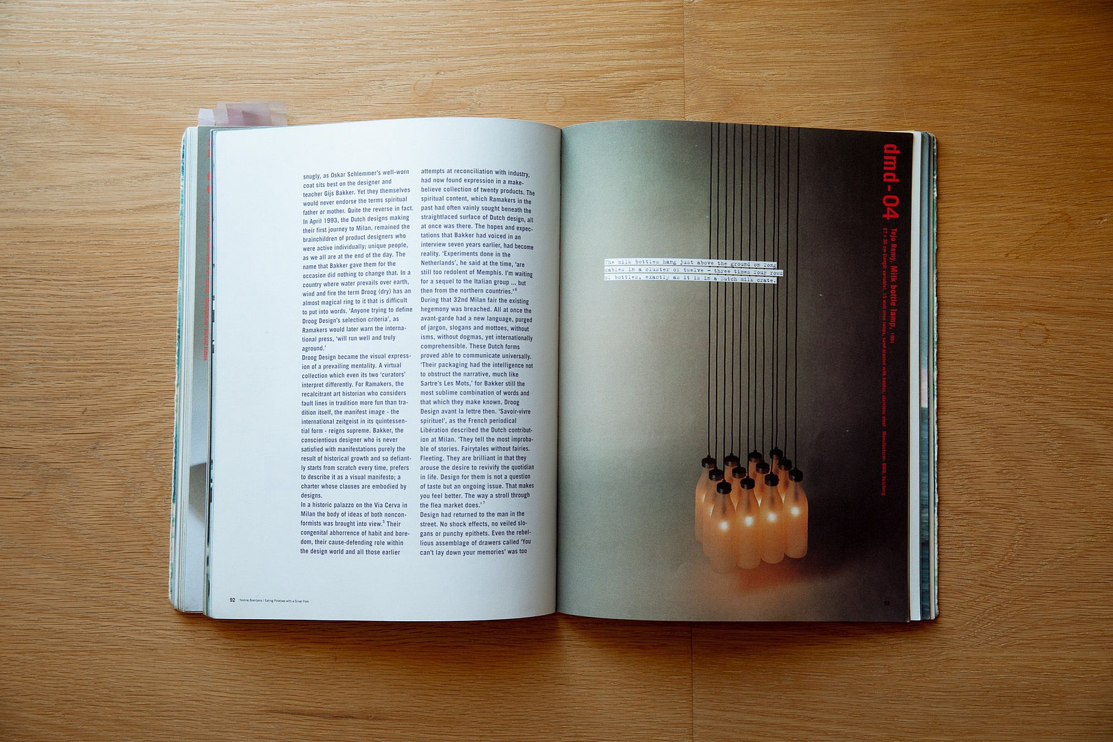Open magazine spread on a wooden table, left page with dense text columns and right page a dark section with red vertical text and hanging light bulbs at the bottom.