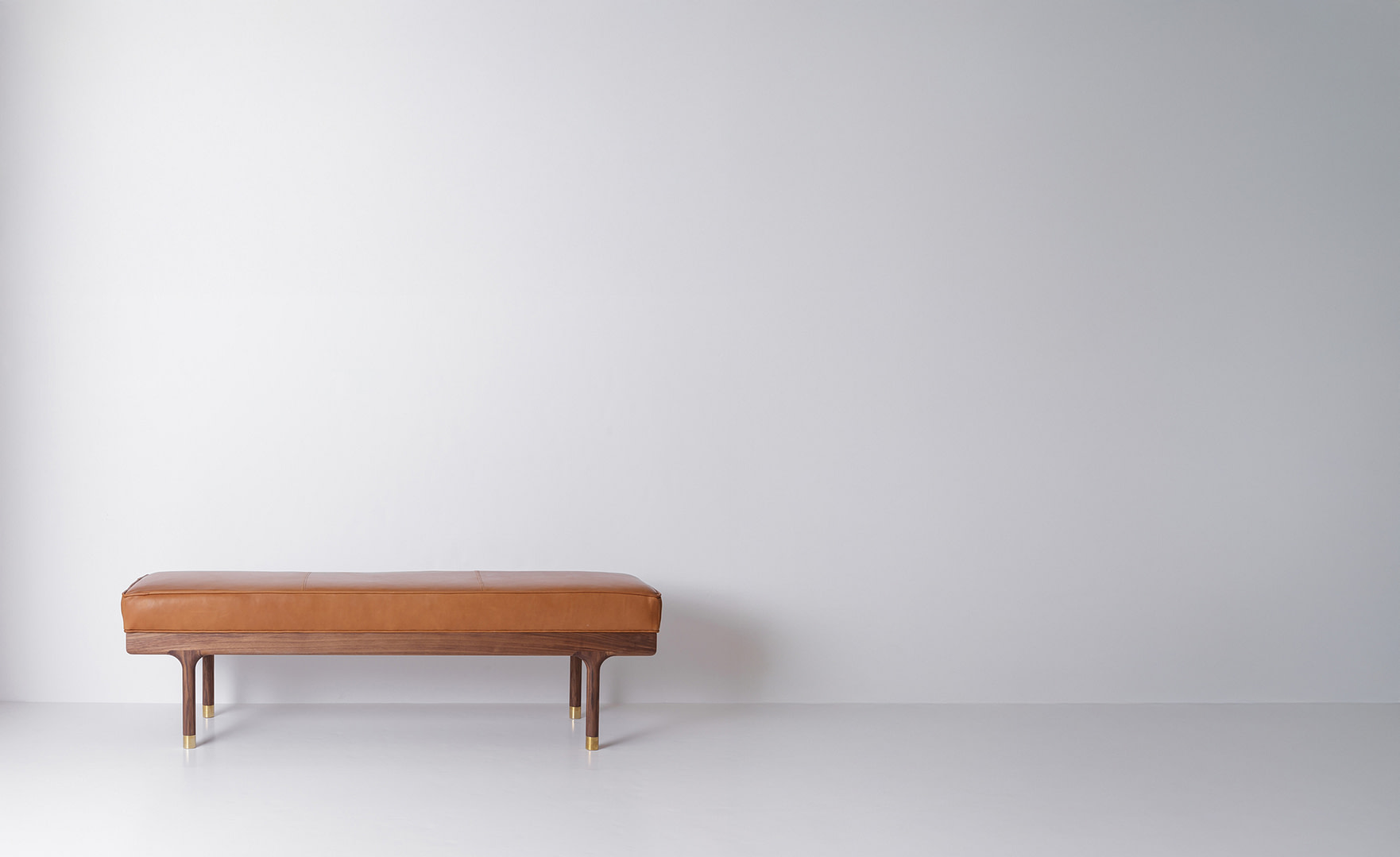 Simple Bench with a tan leather top on a walnut frame, off-center left in a wide frame, turned legs with brass feet.