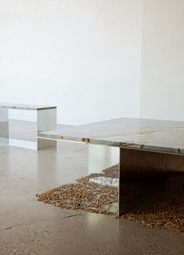 Kalon Material Studies Ii Stone Metal Furniture 7 Minimalist Indoor Scene with Chrome Mirror like Benches and a Spread of Small Gravel Along the Base of a Glass Display Case