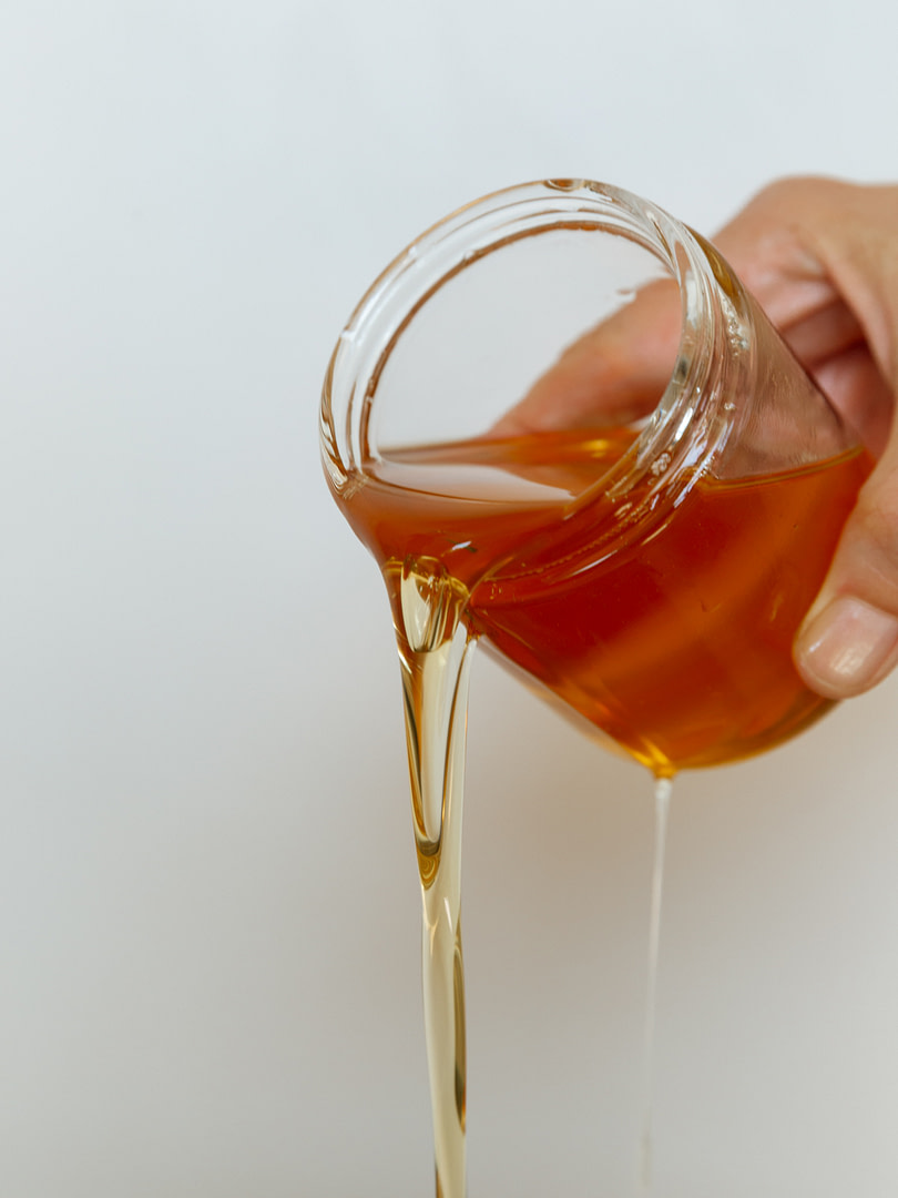 Kalonstudios materials 5 Hand Pouring Amber Caramel Syrup from a Glass Jar Liquid Flowing Downward in Thin Streams