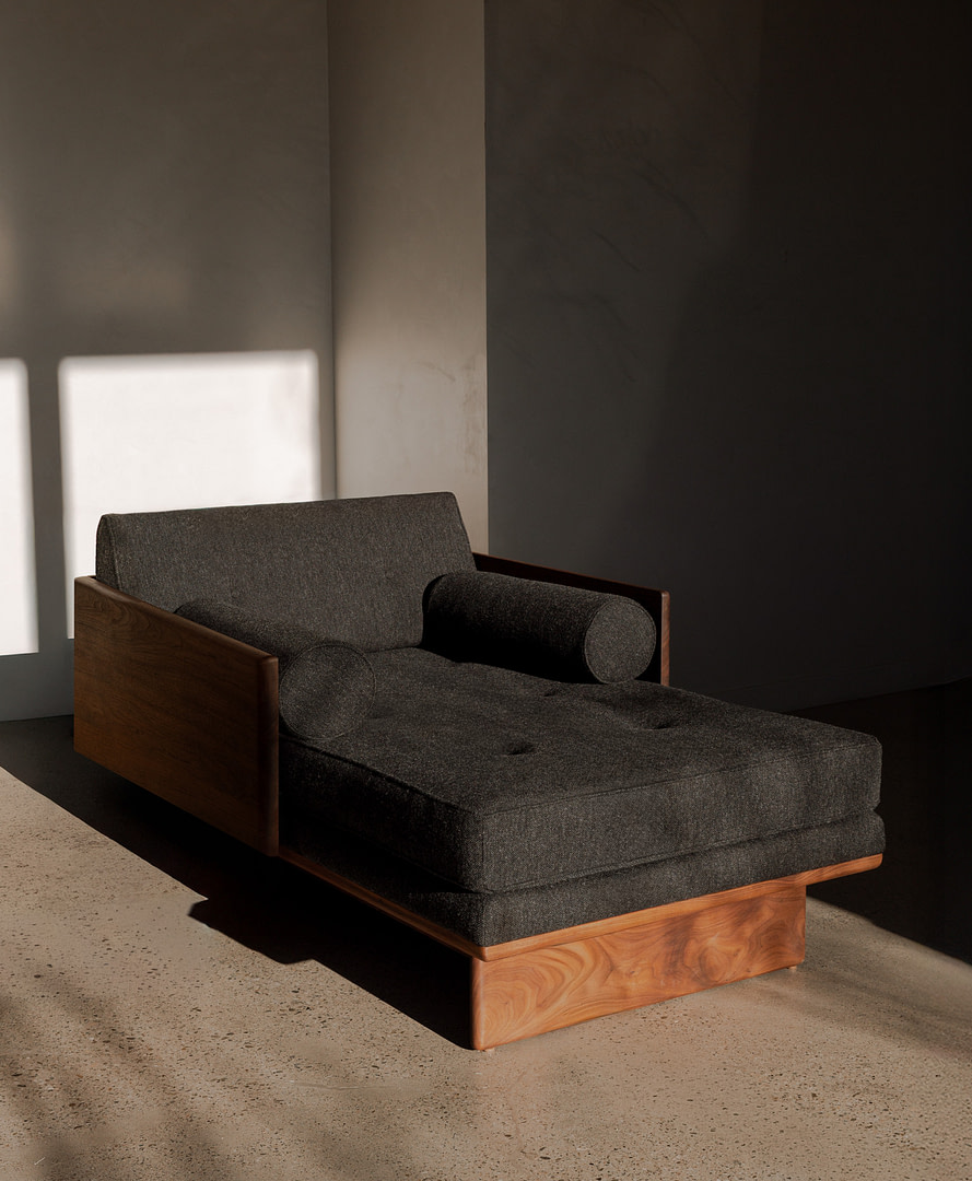Chaise no6 living room wood kalon studios homepage Mid century Grey Upholstered Chaise Lounge with Wooden Arms and Base in a Dimly Lit Room Kalon Studios Creates Contemporary Furniture in Wood Metal Stone and Natural Textiles Designed in Los Angeles Built to Endure Since 2007