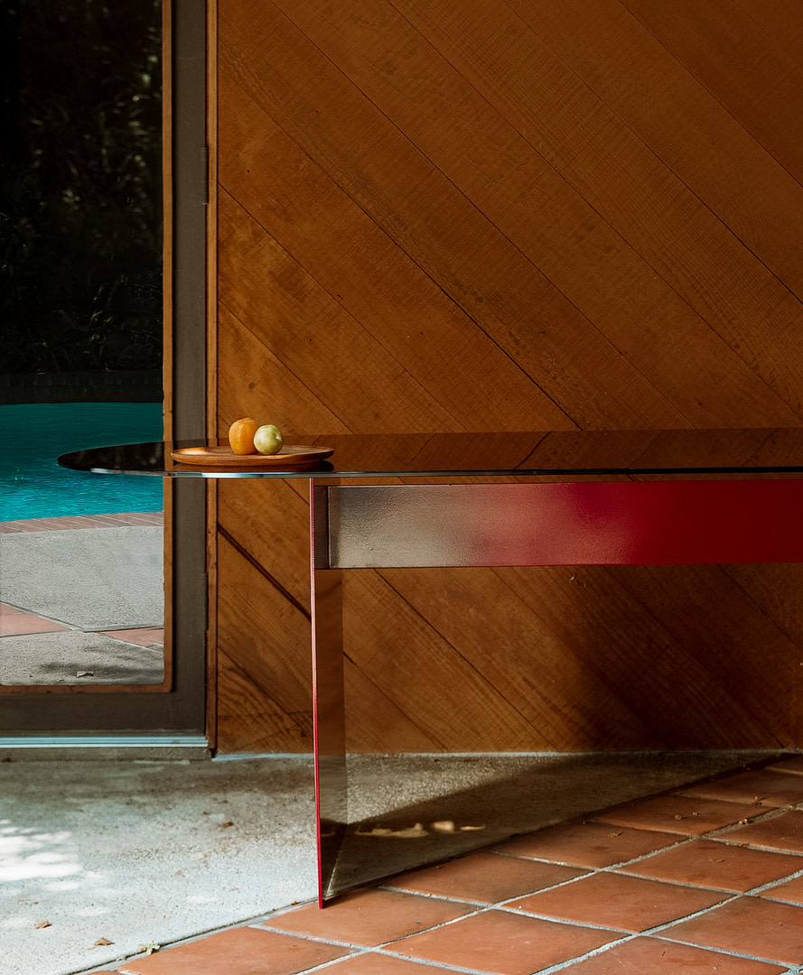 Dining table material studies i outdoor metal aluminum kalon studios homepage Round Glass Table with a Wooden Tray Holding an Orange and a Pale Green Apple Set Against a Diagonal Wood paneled Wall a Glass Door and Outdoor Pool Area Visible to the Left Kalon Studios Creates Contemporary Furniture in Wood Metal Stone and Natural Textiles Designed in Los Angeles Built to Endure Since 2007
