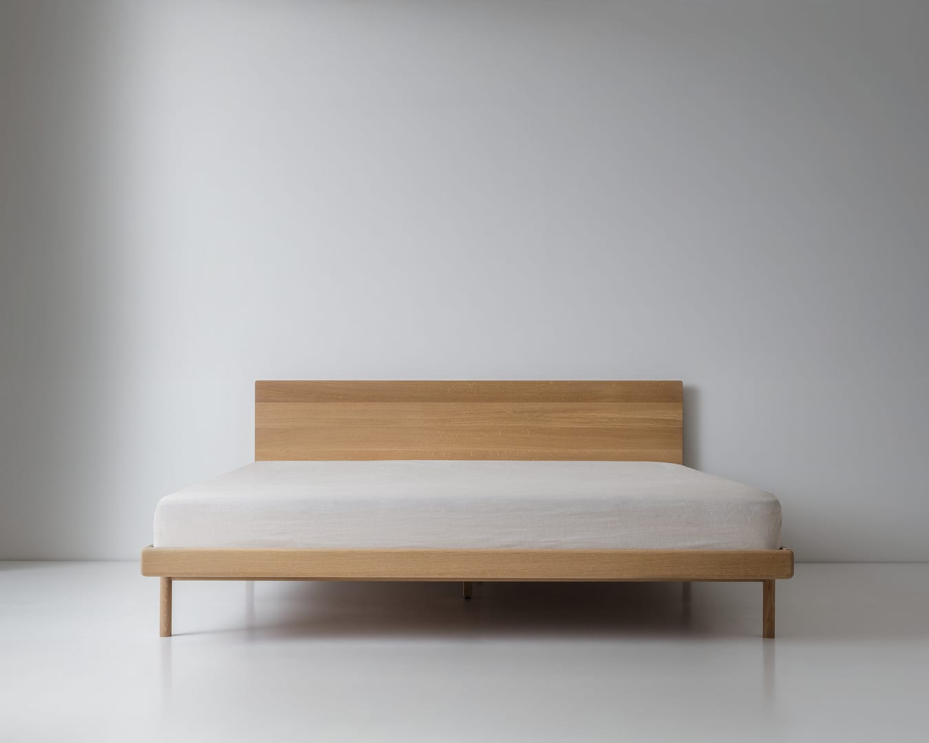 Simple Bed in white oak with panel headboard and white mattress plain wood legs wide centered view generous floor