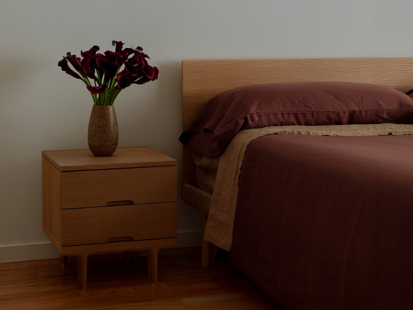 Simple Bed in white oak with burgundy linen bedding the Simple Side Table beside it with calla lilies wood plank floor