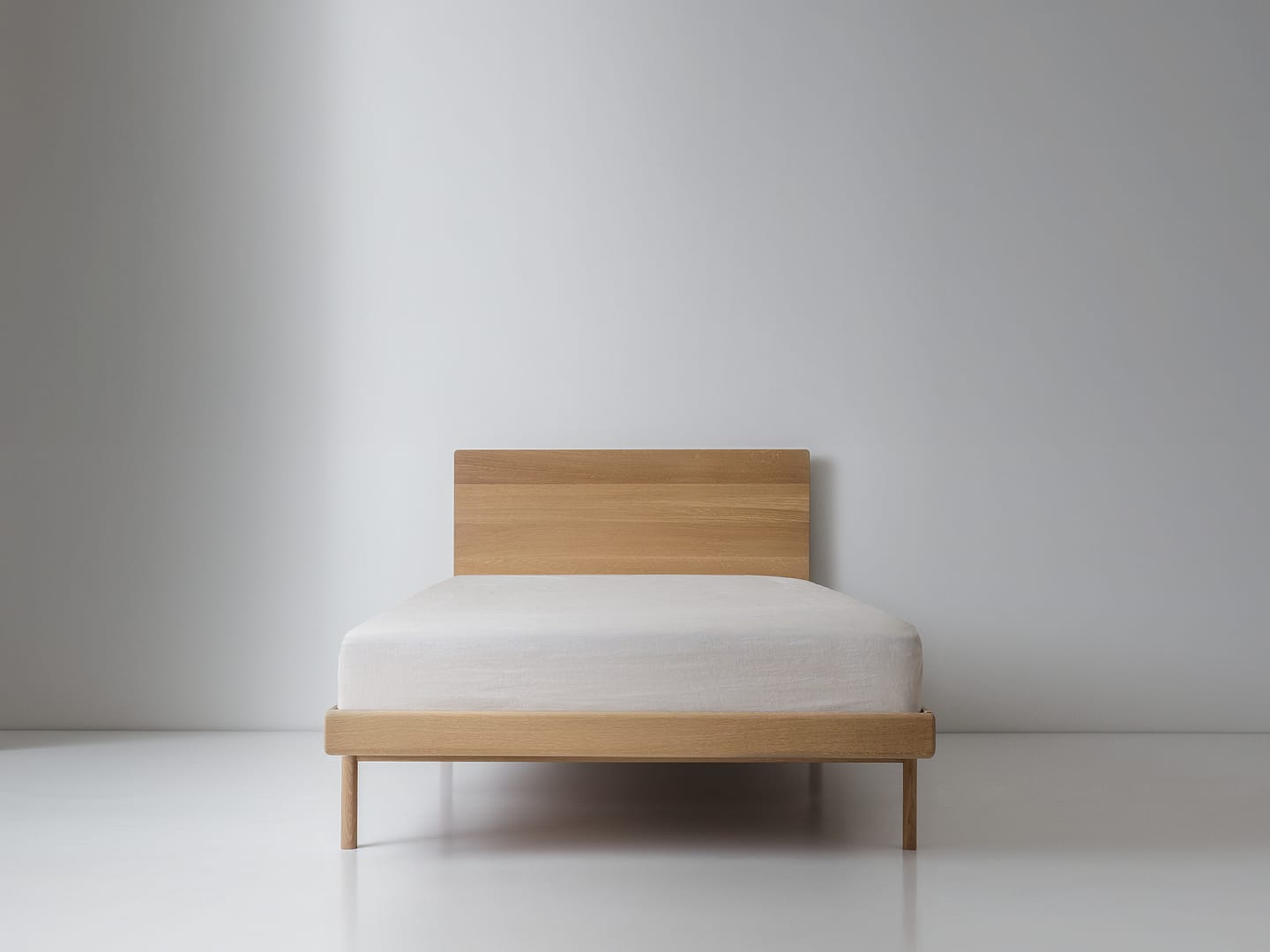 Simple Bed in white oak with panel headboard and white mattress plain wood legs centered front view white floor