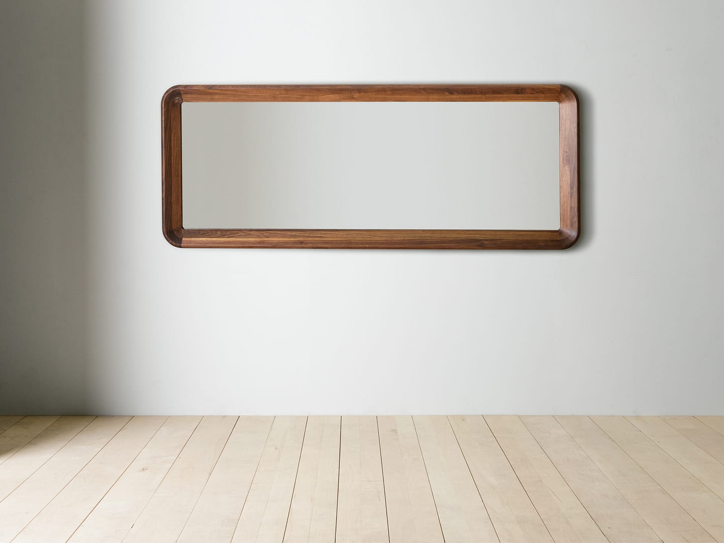 Simple Mirror in walnut mounted horizontally on the wall above a plank floor rounded corner frame figured walnut grain