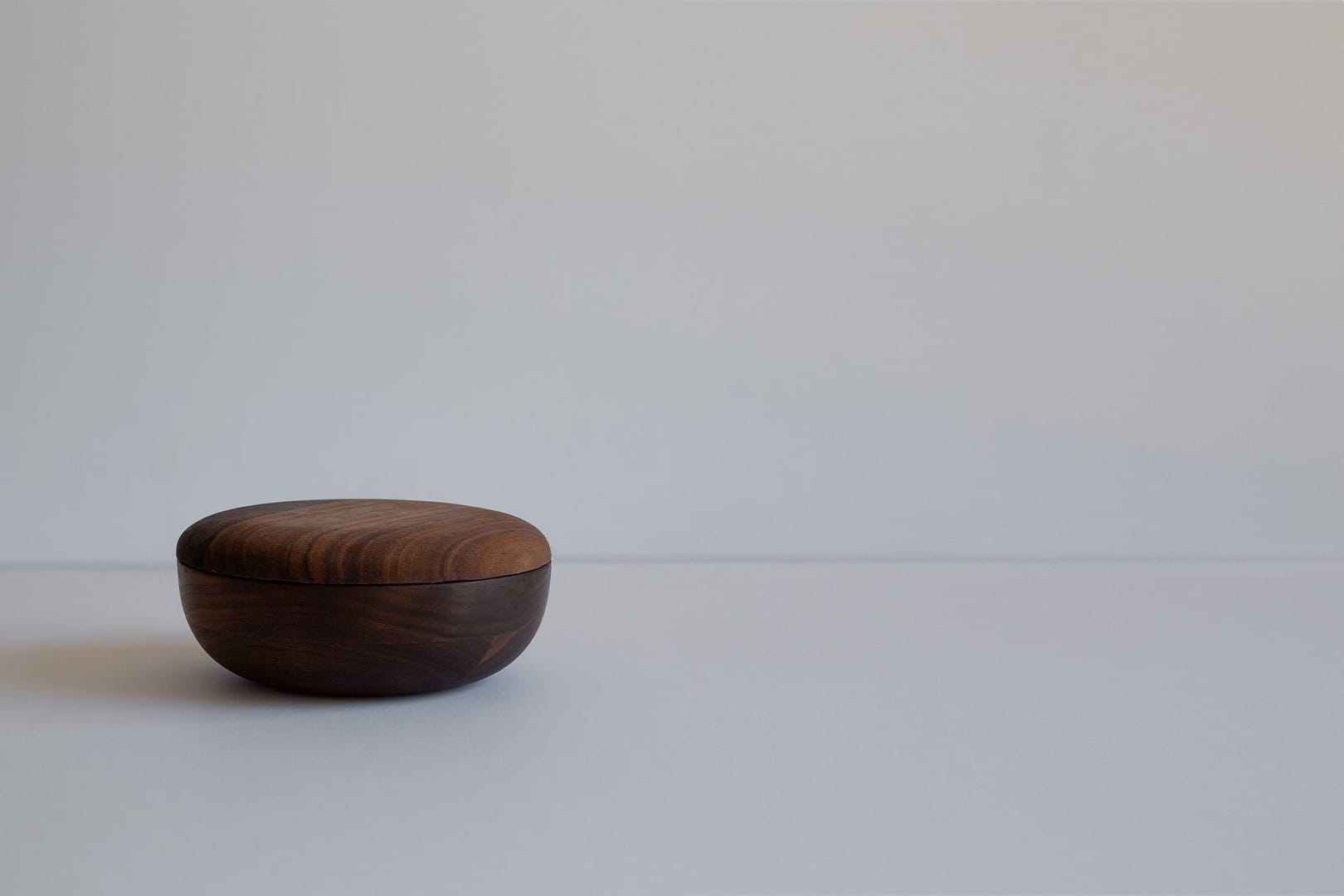 6 inch roasted bowl with lid on a small dark rounded form set to one side of a white field