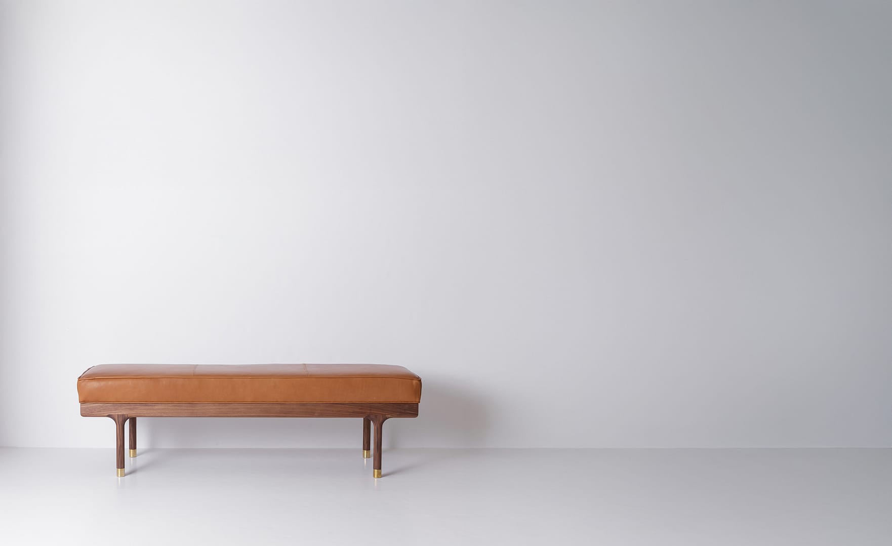 Simple Bench with a tan leather top on a walnut frame off center left in a wide frame turned legs with brass feet