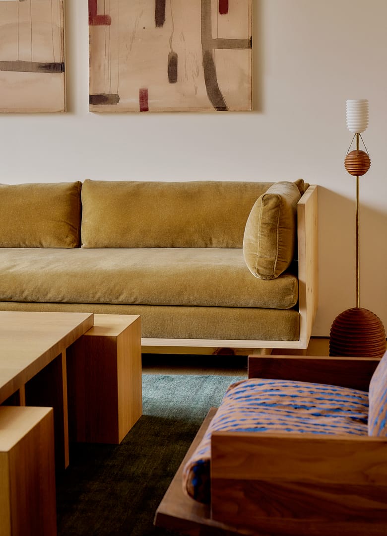 Beige sofa with wooden frame and cushions abstract art on the wall above and a midcentury floor lamp beside it